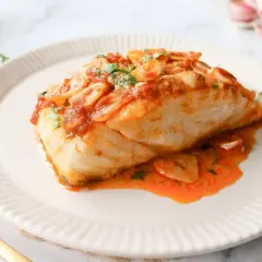 Delicioso bacalao a la llauna con salsa de tomate y ajo, servido en un plato blanco con un tenedor dorado.