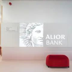 Nowoczesne wnętrze oddziału Alior Bank z logo banku, grafiką i czerwonym pufem.