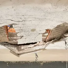 Soffitto sfondato che rivela la struttura del solaio sottostante, con mattoni e armatura a vista.