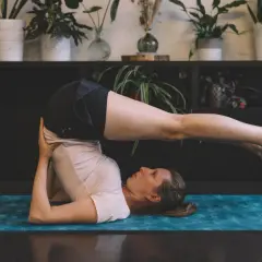 Femme effectuant des étirements du dos sur un tapis de yoga bleu. Ses jambes sont levées et tendues au-dessus de sa tête.