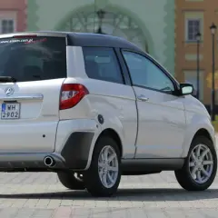Białe auto Aixam GTR, idealne jako auto bez prawka, parkuje na brukowanym placu przed kolorowymi kamienicami.
