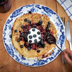 En hög med pannkakor toppas med grädde, blåbär och en generös klick drottningsylt. Perfekt för ett mysigt fika.