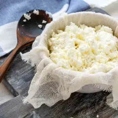 Świeży twaróg z mleka krowiego, odsączany na gazie. Drewniana łyżka obok sugeruje, jak zrobić twaróg w domu.