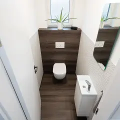 Bagno piccolo con WC sospeso, lavandino bianco e specchio asimmetrico. Un esempio di come piastrellare un bagno piccolo con stile.