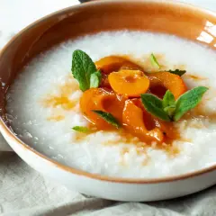Miseczka z kremowym congee, ozdobiona kawałkami brzoskwini i listkami mięty.