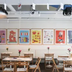 Bunte Bilder zieren die Wand im theater la lune Stuttgart. Kleine Tische mit Blumen laden zum Verweilen ein.