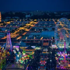 Nocne, rozświetlone atrakcjami wesołego miasteczka, gdzie trwa **feria de abril**. Widać diabelski młyn, kolejki górskie i tłumy ludzi.