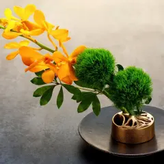 Elegante Ikebana Beispiele: leuchtend orangefarbene Orchideen und zwei grüne, kugelförmige Blüten auf einem dunklen Teller in einem kunstvollen goldenen Halter.