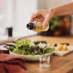 Frische Salatblätter werden mit einem Dressing beträufelt. Rotweinessig ist eine gesunde Wahl, besonders in der Schwangerschaft.