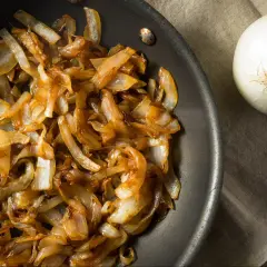 Złocista, aromatyczna karmelizowana cebula na patelni, obok świeżej cebuli. Idealna do burgerów i zapiekanek.