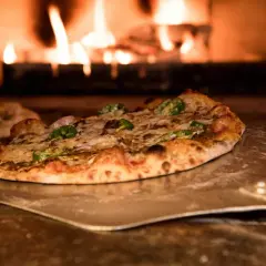 Pizza na łopacie przed palącym się piecem.