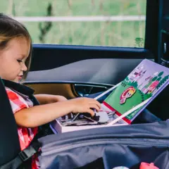 Dziewczynka w foteliku samochodowym bawi się naklejkami z księżniczką, szukając zabawy na nudę w podróży.