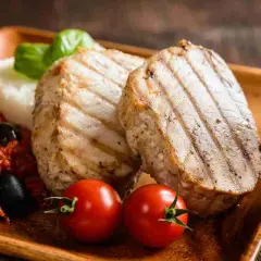 Delizioso tonno alla piastra con contorno di riso, pomodorini, olive e basilico su un piatto di legno.