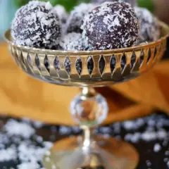Nyttiga chokladbollar rullade i kokosflingor, serverade i en vacker guldfärgad skål. En perfekt, hälsosam godsak!