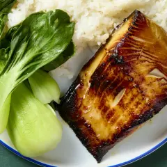 A glistening piece of black cod, marinated and seared to perfection, sits beside fluffy white rice and vibrant green bok choy.