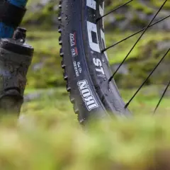 Close-up of a muddy bike tire, showing the "Maxxis Ikon" branding. This tire is ready for a challenging trail review.