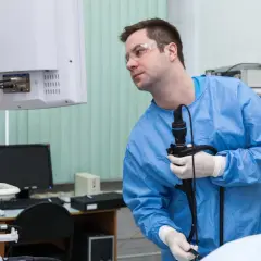 Lekarz w niebieskim fartuchu i okularach ochronnych trzyma endoskop, przygotowując się do badania. Czy gastroskopia boli? Procedura jest zazwyczaj bezbolesna.