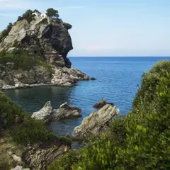 Felsige Klippe mit weißem Haus und Bäumen, umgeben von üppiger Vegetation und dem blauen Meer. Hier wurde Mamma Mia gedreht.