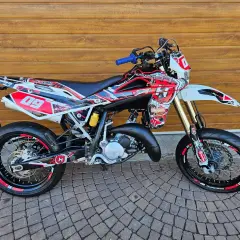 Husqvarna TE 125 z agresywnym oklejeniem w czerwono-białe wzory, gotowa do jazdy po torze.