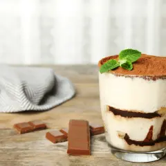 Szybki deser z niczego: kremowe tiramisu w szklance, posypane kakao i udekorowane miętą. Obok kawałki czekolady.