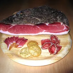 Ein Stück italienischer Speck mit Scheiben und Keksen auf einem Holzbrett.