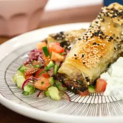 Krispig spenat och fetaostpaj toppad med sesamfrön, serverad med en fräsch tomatsallad och tzatziki.