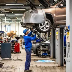 Mekaniker arbetar under en bil på en lyft i en auktoriserad verkstad. Verkstaden är välutrustad med verktyg och maskiner.