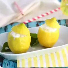 Deux citrons évidés remplis de sorbet citron, servis sur une assiette blanche, avec des feuilles vertes et des pailles colorées en arrière-plan.