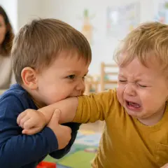Chłopiec gryzie ramię innego dziecka, które płacze. Widać, że dziecko nie radzi sobie z emocjami.