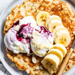 Puszysty omlet z bananem, udekorowany bitą śmietaną, musem jagodowym i płatkami migdałów. Idealne śniadanie.