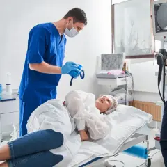 Przygotowanie do kolonoskopii ze znieczuleniem na NFZ. Lekarz w niebieskim fartuchu trzyma sprzęt, pacjentka leży na łóżku.