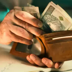 Dłonie wkładają polskie banknoty do brązowego portfela. Może to być pomoc w opłaceniu rachunków, np. bon ciepłowniczy.
