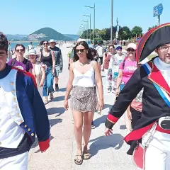 Gente pasea por el paseo marítimo de Santoña, algunos disfrazados, disfrutando del sol y el ambiente festivo.