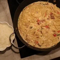 En stor panna med krämig pasta med baconsås. Bredvid en skål med riven ost.