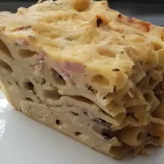 Kawałek zapiekanki makaronowej z serem i szynką na talerzu.