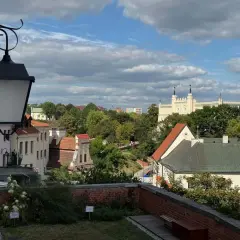 Widok na Lublin na weekend. Zabytkowe kamienice, zieleń i biały zamek na wzgórzu pod błękitnym niebem.