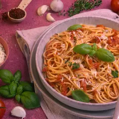 Ein Teller Spaghetti Napoli mit Tomatensauce, Basilikum und Parmesan. Daneben frische Tomaten, Knoblauch und Kräuter.