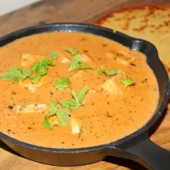 En krämig paneer-rätt i en gjutjärnspanna, garnerad med mynta. Bredvid ligger två gyllene, tunna bröd. Ett perfekt paneer recept!