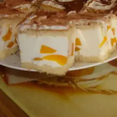Sernik z bitą śmietaną siostry Anastazji, z kawałkami brzoskwini, posypany kakao. Pyszny deser na talerzu.