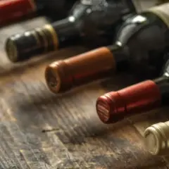 Rząd butelek wina na drewnianym stole. Zastanawiasz się, czy można pić wino po terminie przydatności na butelce?
