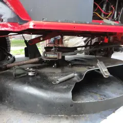 Podczas naprawy traktorka, widać mechanizm kosiska z pasem napędowym i sprężyną.