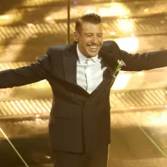 Un artista sorridente sul palco di Sanremo, con microfono in mano, pronto per i duetti.