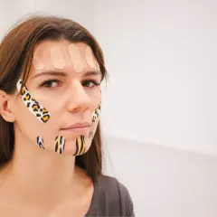 Kobieta z kolorowymi plastrami na twarzy, stosuje taping twarzy dla poprawy wyglądu.