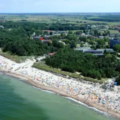 Dąbki: warto jechać! Tłumy ludzi na plaży, zielone lasy i budynki kurortu. Idealne miejsce na wakacje.