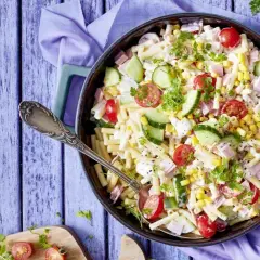 Ein köstlicher nudelsalat mit schinken, garniert mit Kirschtomaten, Gurkenscheiben und Mais. Perfekt für ein Sommerfest!
