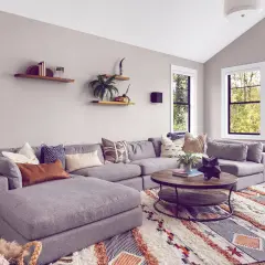 Gemütliches Wohnzimmer mit großem Ecksofa, Kaffeetisch und einem auffälligen Teppich im Boho-Stil, der den aktuellen Teppich Trend widerspiegelt.