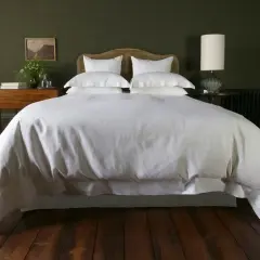 A white duvet cover, resembling a plush bedspread, drapes over a neatly made bed, contrasting with the crisp bed sheet visible beneath.