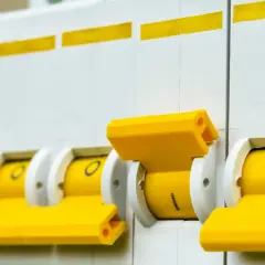 Rząd żółtych dźwigni wyłączników nadprądowych, pokazujący różne rodzaje bezpieczników w akcji.