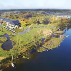 Malownicze miejscowości na Mazurach: hotel nad jeziorem, otoczony zielenią i jesiennymi drzewami. Drewniane pomosty zapraszają do wodnych przygód.