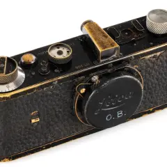 Czarny, zabytkowy aparat Leica z widocznymi śladami użytkowania, jeden z najdroższych starych aparatów fotograficznych, z wygrawerowanym napisem "OSCAR BARNACH".